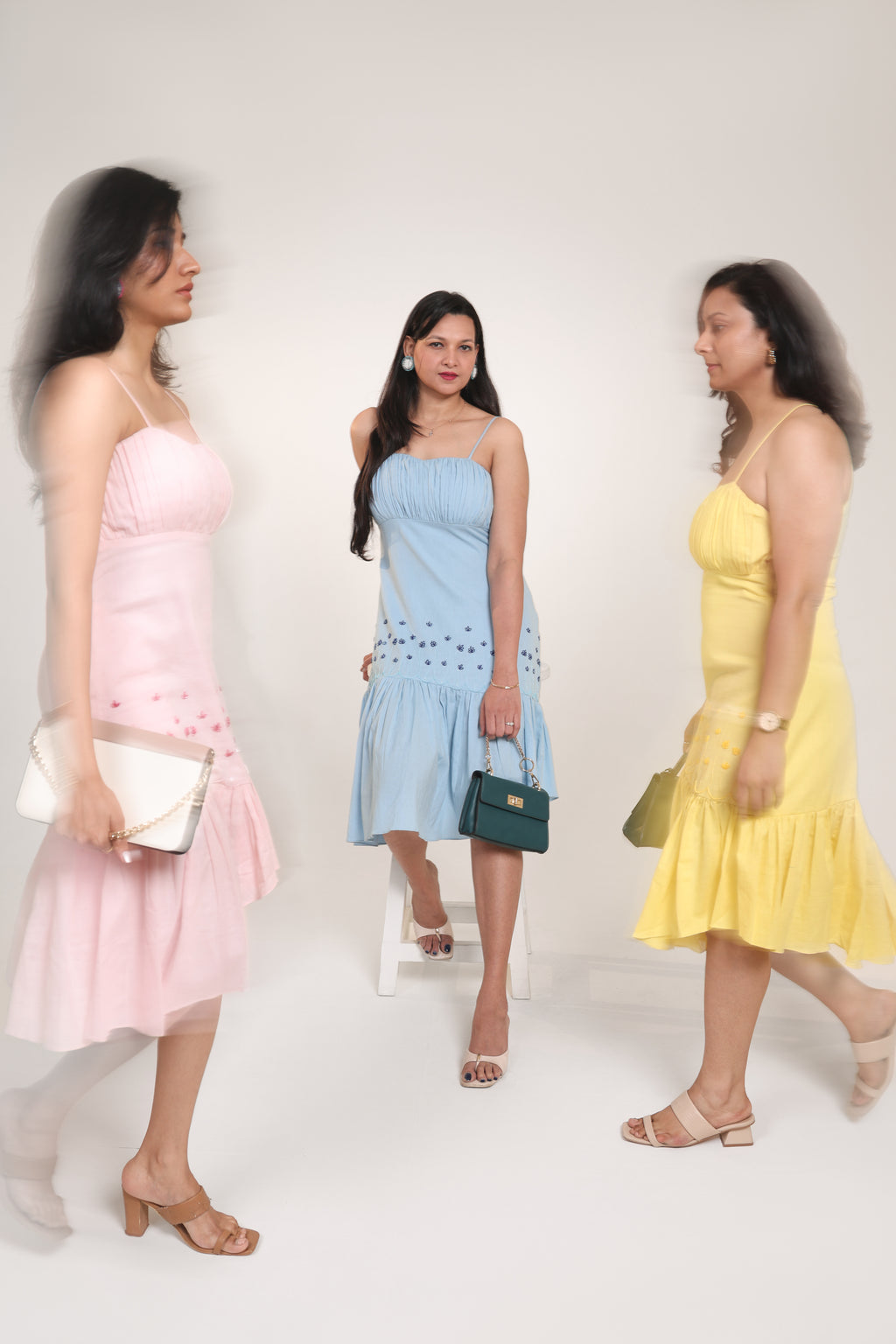 Three women wearing Pink Yellow and Blue dresses with handbags on a white background